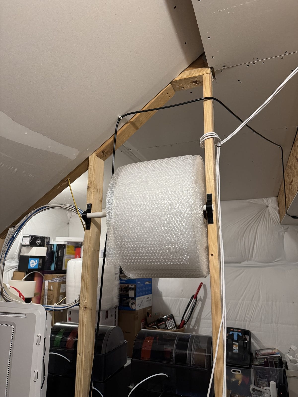 A bubble-wrap roll on a 3D-printed wall dispenser above the packing bench