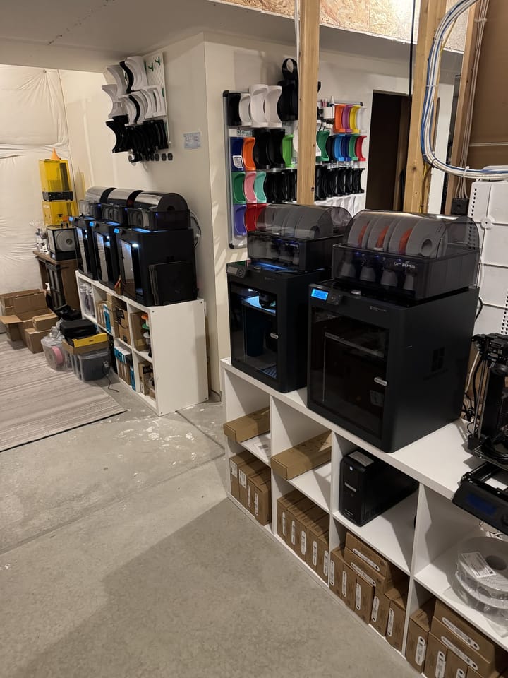 The DrawnToCreations print farm: Bambu Lab P1S printers with AMS units and mount inventory